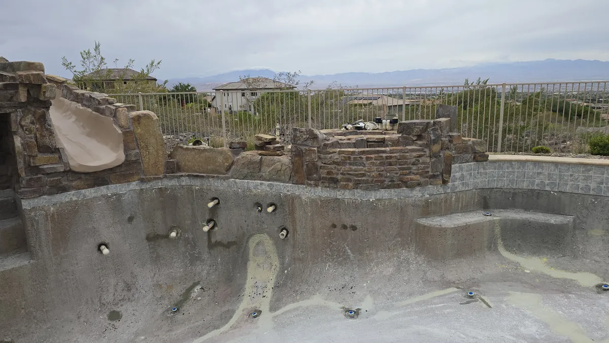 Drained pool with exposed spa fittings, stonework and a slide during remodeling.
