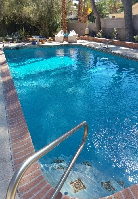 Metal handrail beside tiled steps into a residential pool.