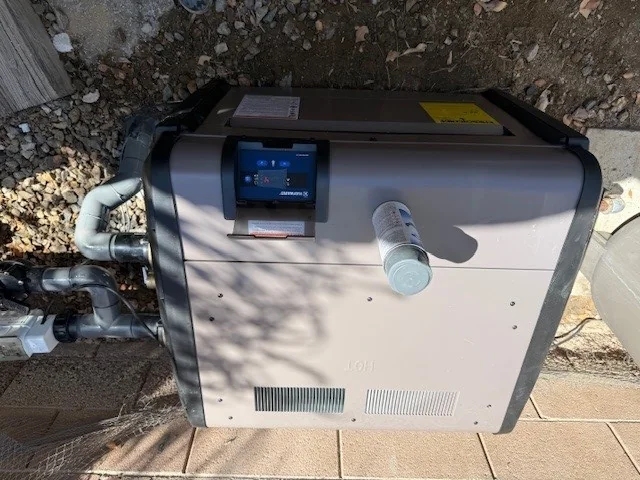 Pool heater beside pipe connections at a residential equipment pad.