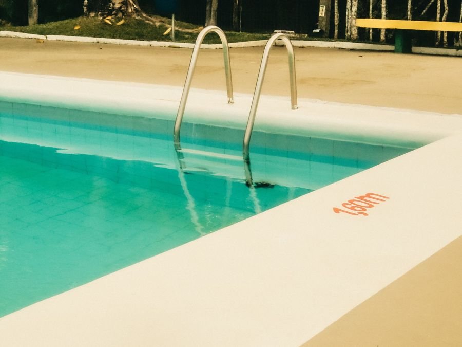 Pale pool coping beside green-blue water and ladder rails.
