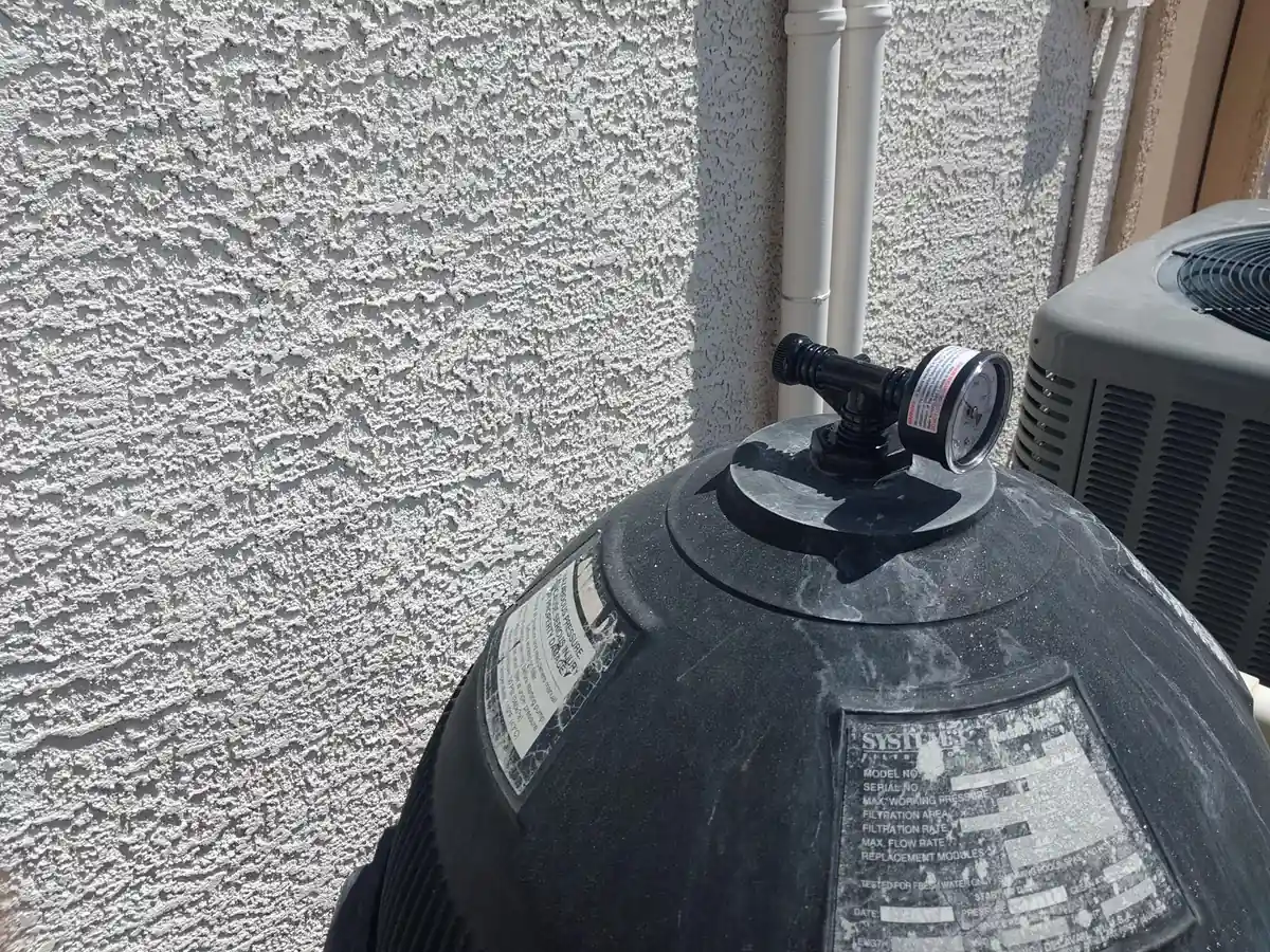 Dark filter tank with its pressure gauge beside an equipment wall.