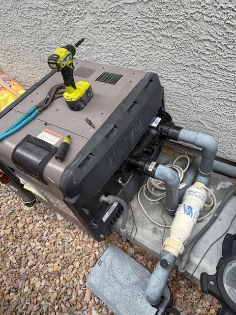 Cordless drill on a pool heater beside connected plumbing.