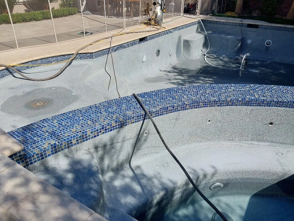 Blue tile and coping around a drained spa during tile-cleaning work.