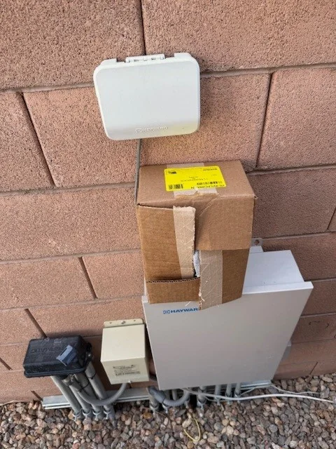 Outdoor pool control panels mounted on a wall.
