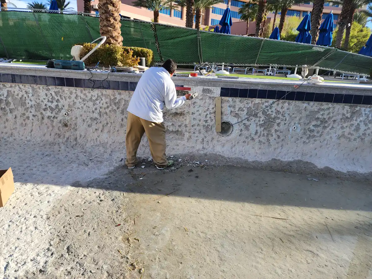 Worker removing tile from the inside wall of a drained pool.