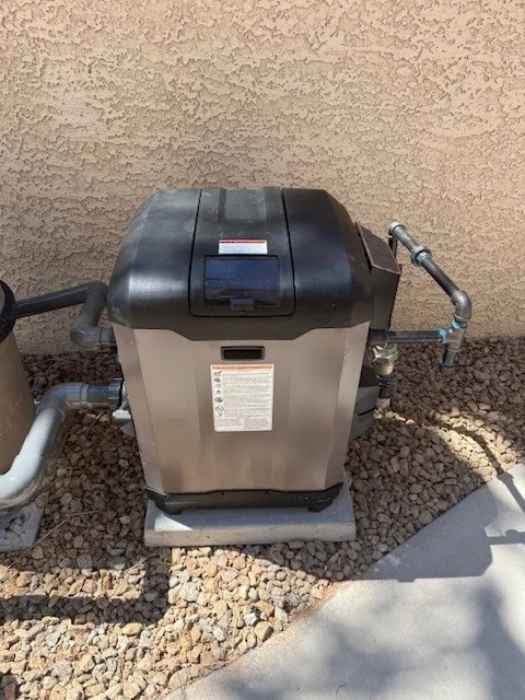 Pool heater connected to pipes on an outdoor equipment pad.