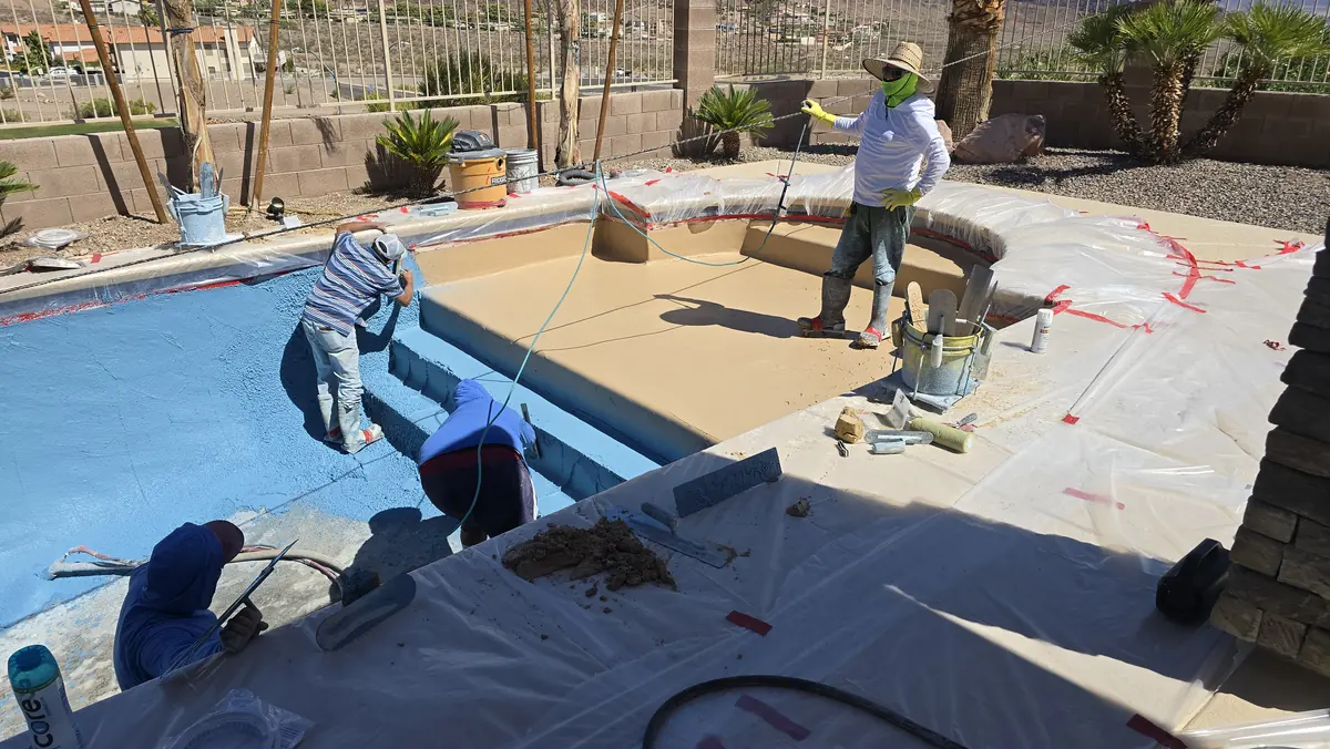 Crew working on the interior surface of a drained residential pool.