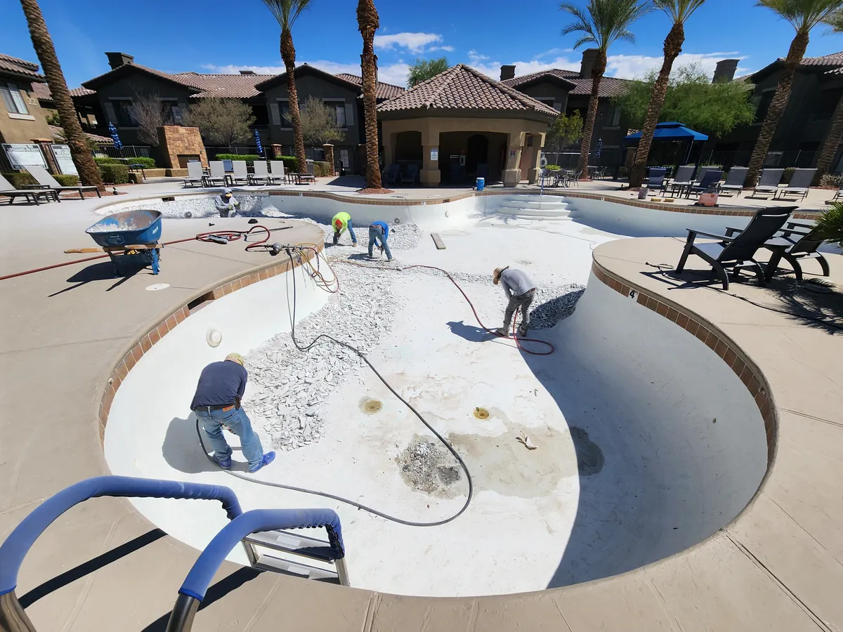 Crew preparing the surface of a drained commercial pool.