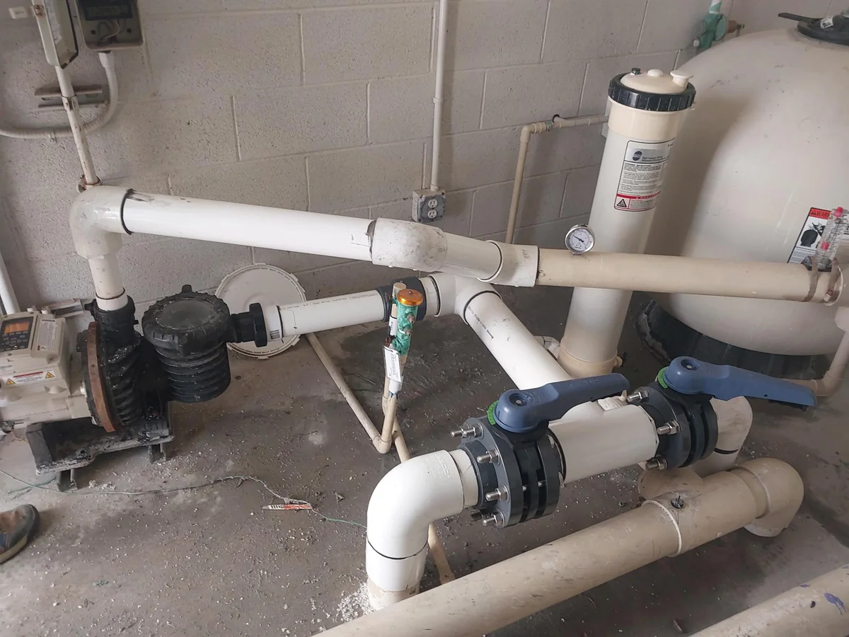 Pool pump plumbing beside a filter tank.