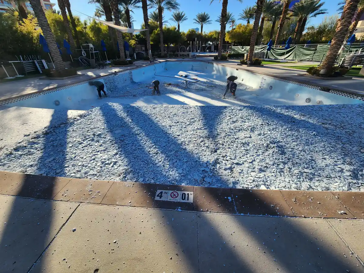 Workers preparing the floor of a drained pool in afternoon light.