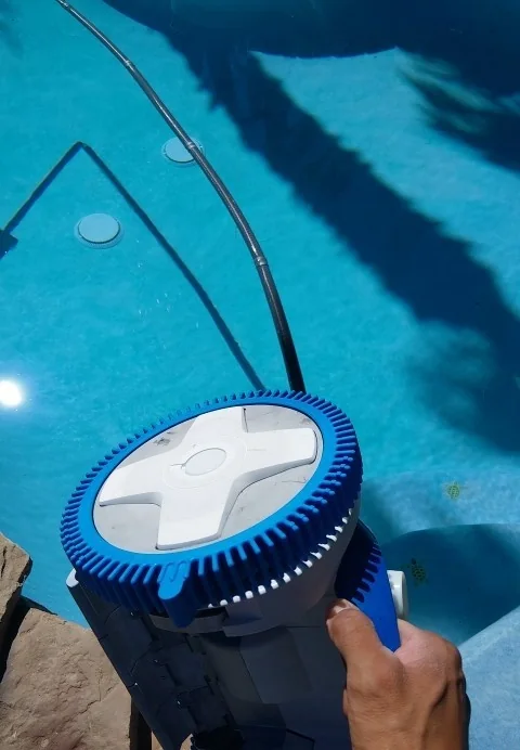 A pool vacuum head held beside the water.
