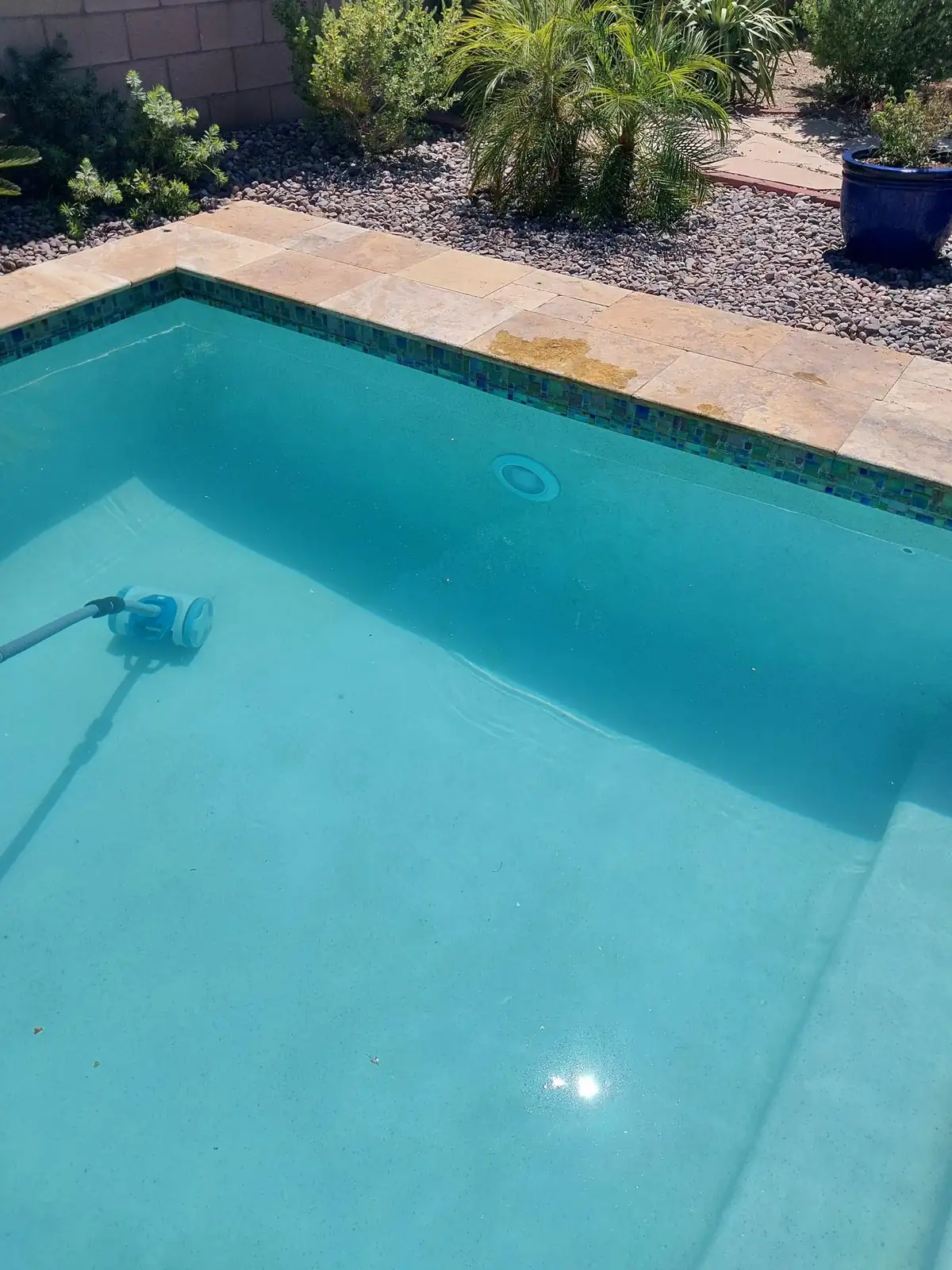 Underwater pool wall light and a cleaner hose beneath the water.