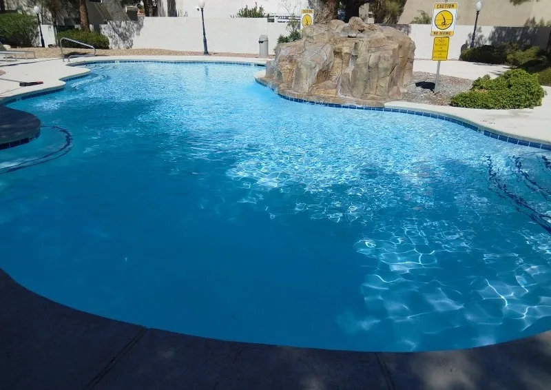 Clear outdoor pool water beside a rock waterfall and surrounding deck.