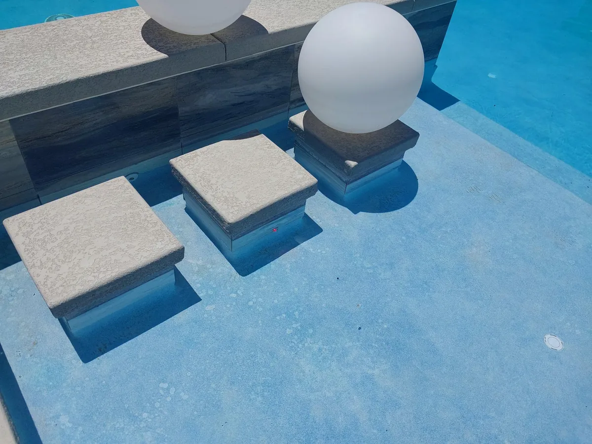 Pool entry steps and a shallow shelf beside a white spherical deck feature.