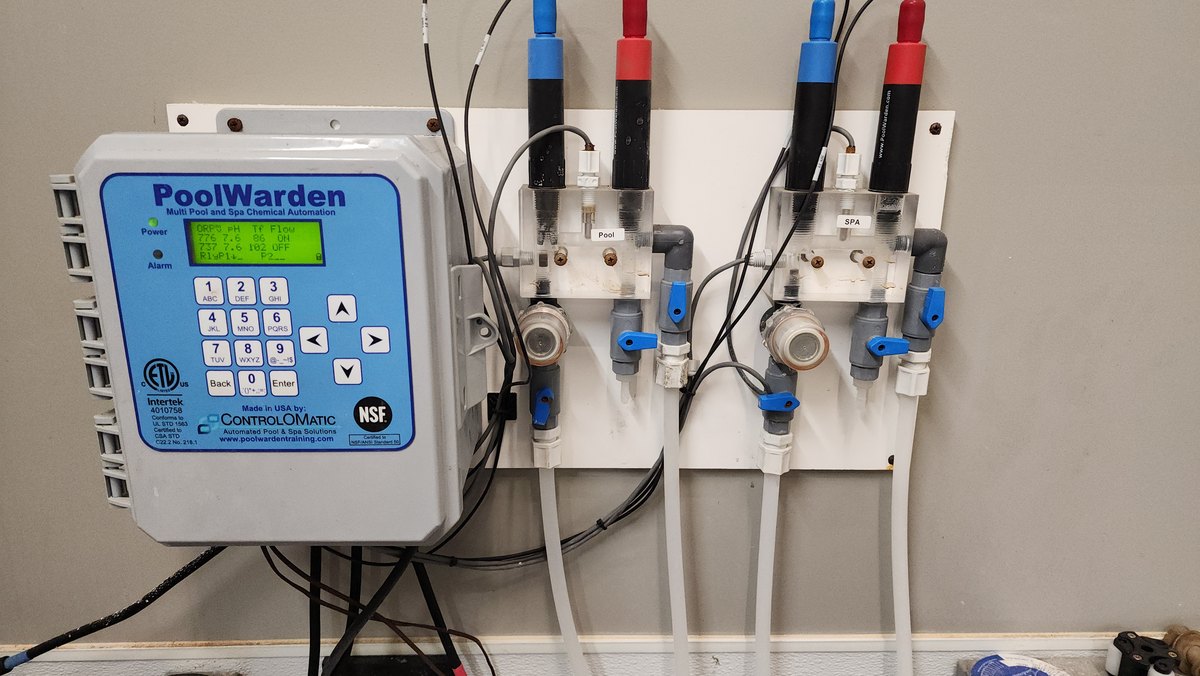 Wall-mounted chemical automation controller beside two sensor assemblies labeled pool and spa.